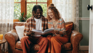 A happy couple, who are intended parents with Babytree Surrogacy, enjoys a quiet moment together reading and smiling. The scene shows warmth and hope during their surrogacy journey. babytree